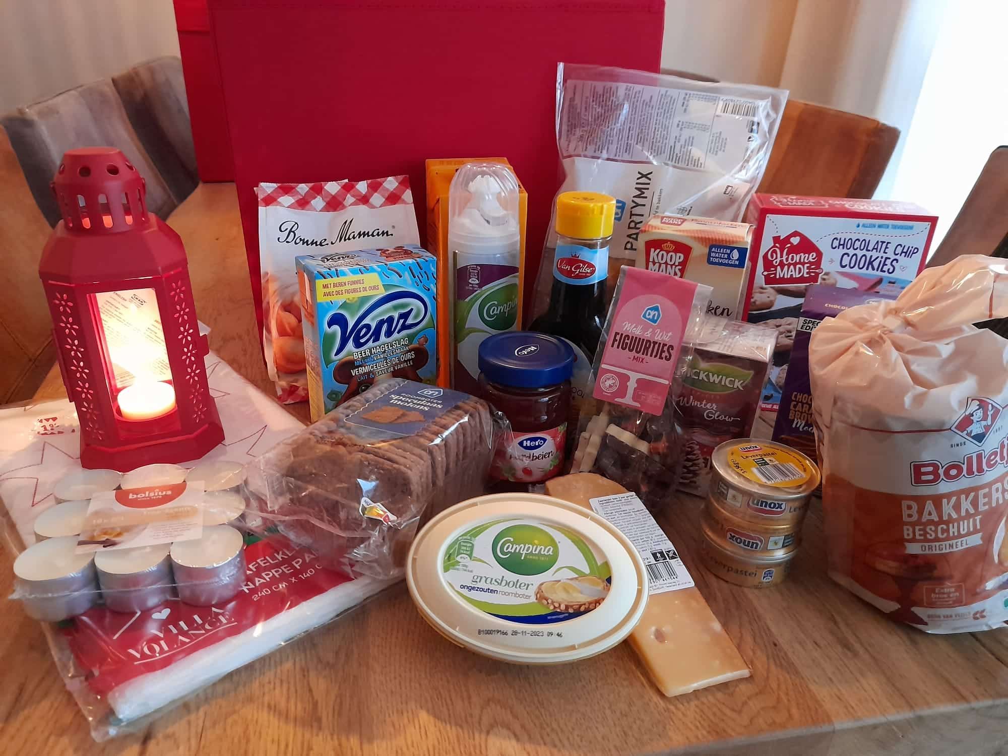 De inhoud van een kerstpakket uitgestald op tafel: houdbare levensmiddelen, koffie en een kaarsenlantaarn