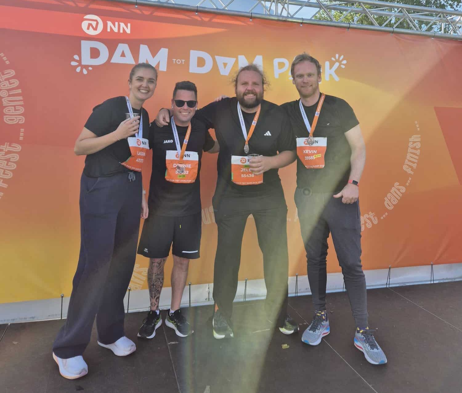 Vier lopers met medailles om de nek voor de banner van de Dam tot Damloop