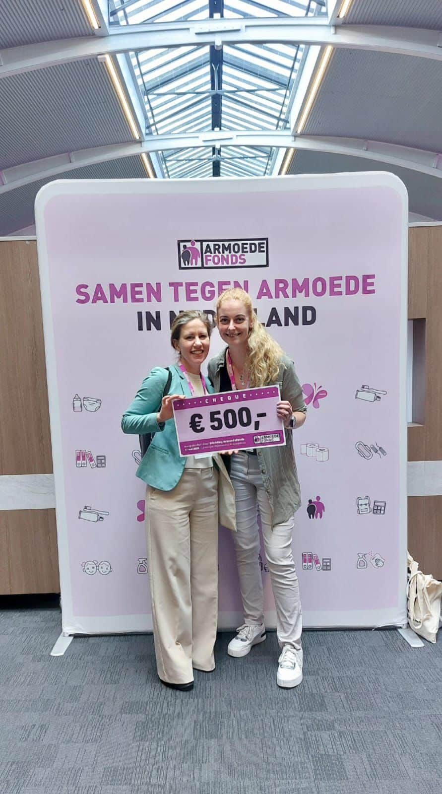 Twee vrouwen houden een cheque van 500 euro omhoog voor een banner van het Armoedefonds