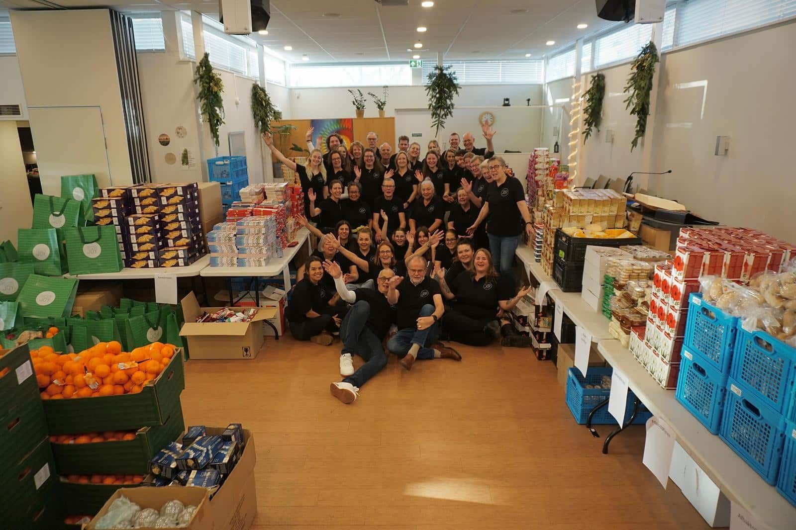 Een grote groep vrijwilligers in de uitgifteruimte, omringd door kratten met boodschappen
