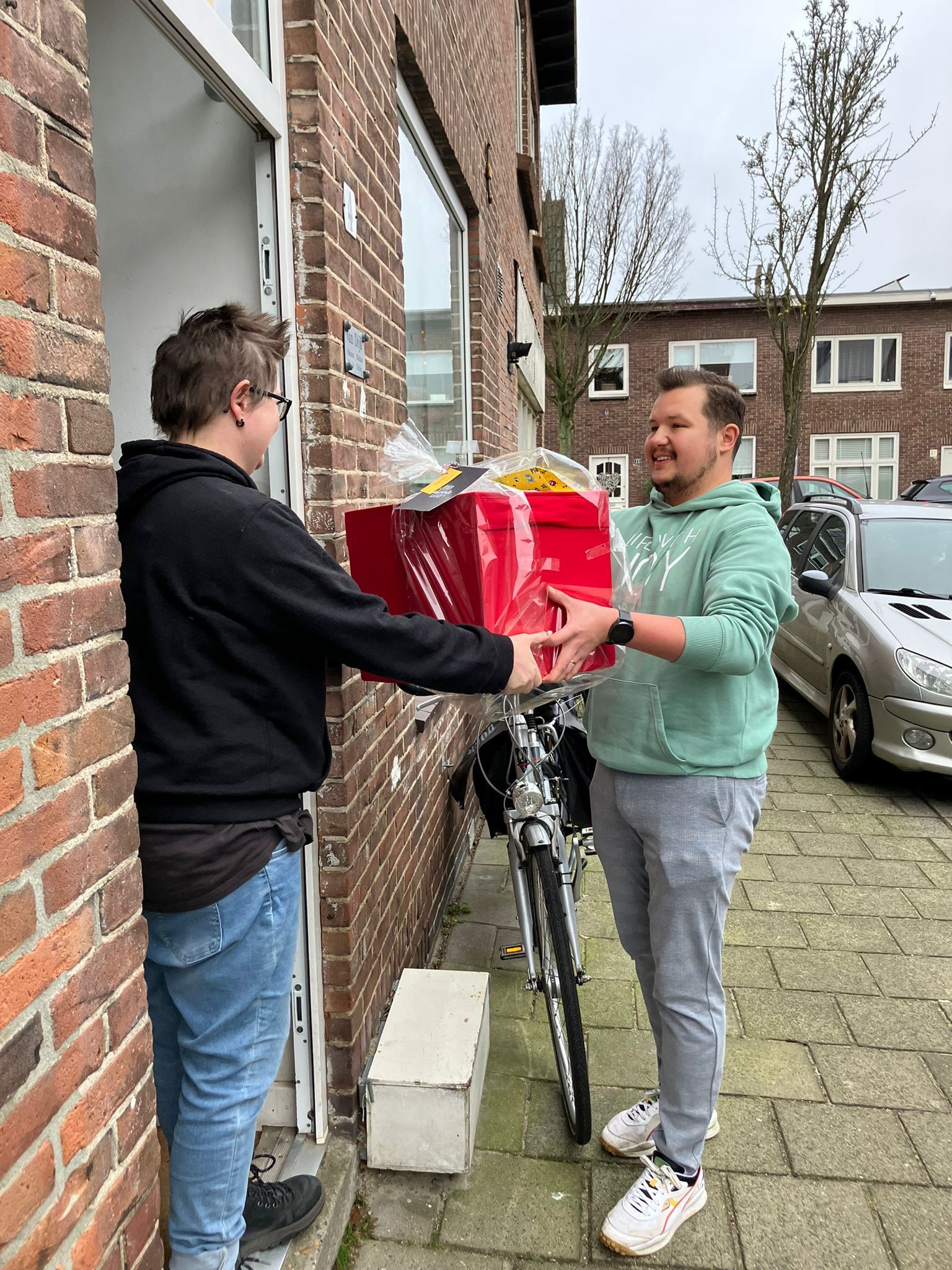 Een vrijwilliger overhandigt een rood ingepakt kerstpakket bij de voordeur