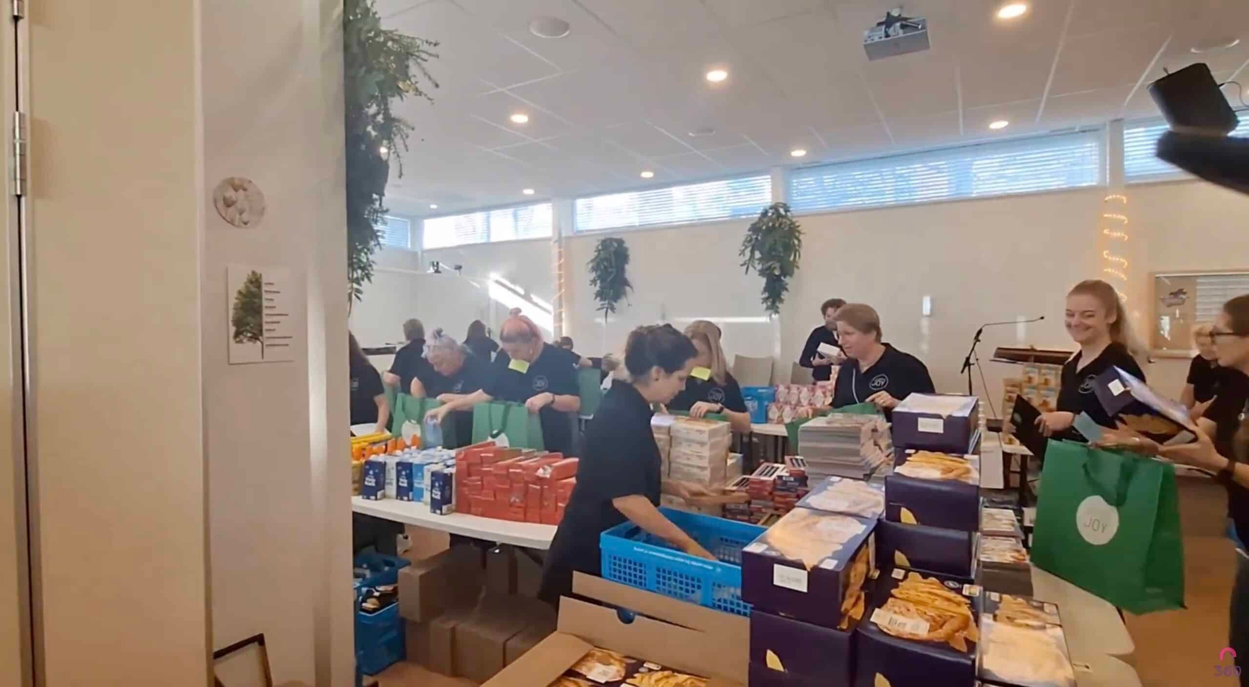 Vrijwilligers stellen aan lange tafels kerstpakketten samen